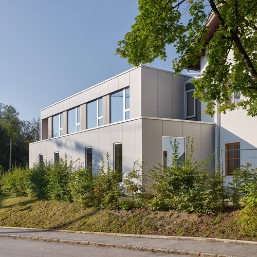 Außenansicht der neuen Erweiterung der Volksschule Neumarkt mit Bäumen im Vordergrund