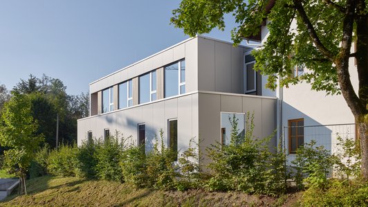 Außenansicht der neuen Erweiterung der Volksschule Neumarkt mit Bäumen im Vordergrund