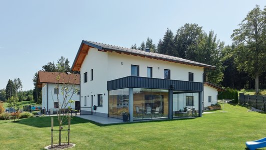 Massivhaus aus Ziegel und Holz mit Wintergarten - Außenansicht mit Wintergarten und Garten