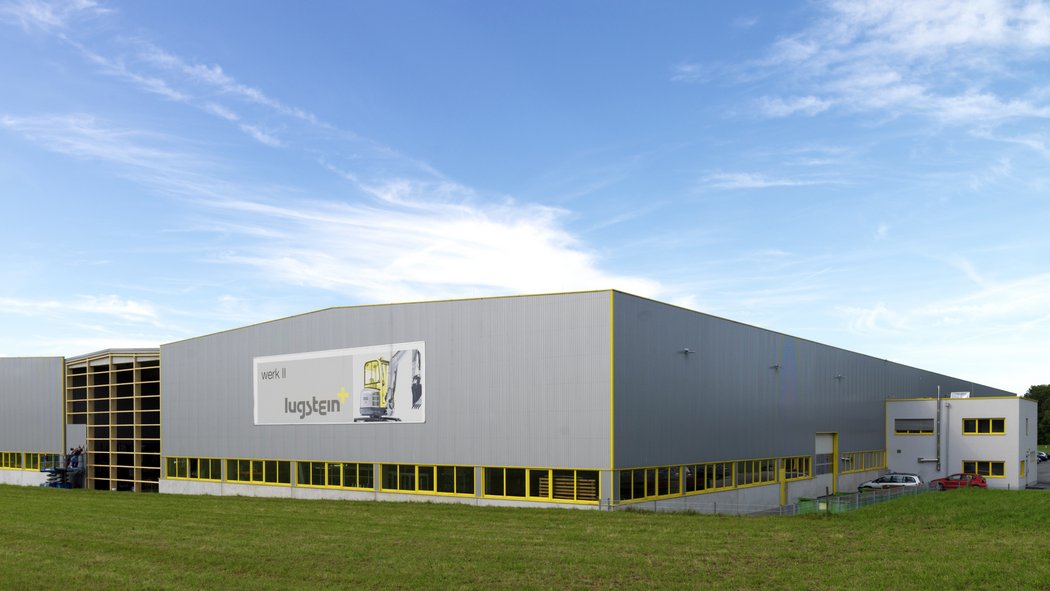 Außenansicht der Lugstein Fahrerkabinen Produktionshalle, mit grauer Fassade und gelben Akzenten, umgeben von einer Wiese