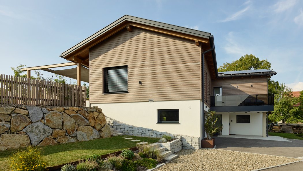 Seitliche Ansicht eines Hauses mit Natursteinmauer und Terrassenbereich