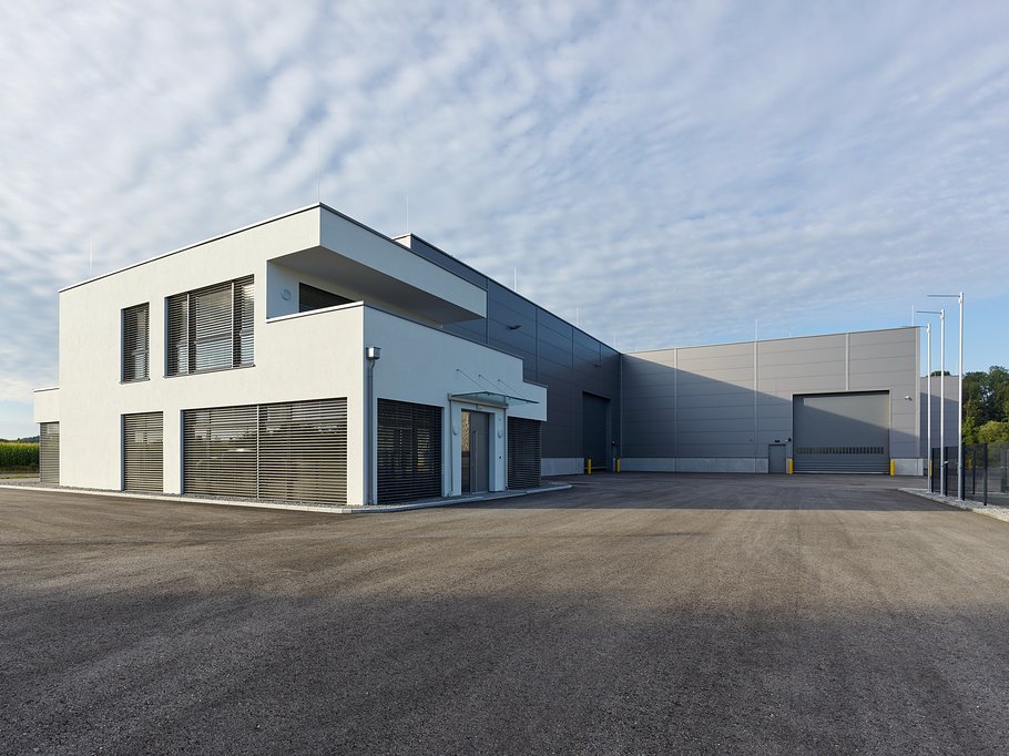Großes weißes Nebengebäude mit modernen Lamellenfenstern, mit weitläufiger Auffahrt, Lagerhalle im Hintergrund