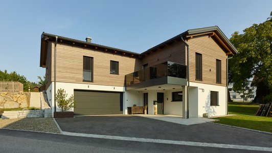 Vorderansicht eines Einfamilienhauses mit Holzfassade und großzügiger Auffahrt