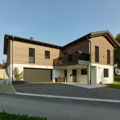 Vorderansicht eines Einfamilienhauses mit Holzfassade und großzügiger Auffahrt