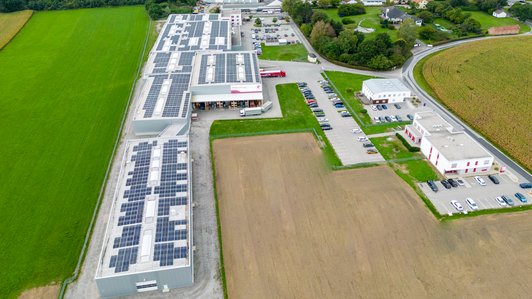 Komplettansicht des Promotech-Betriebsgebäudes mit Solaranlagen, Parkplatz und umliegender Landschaft
