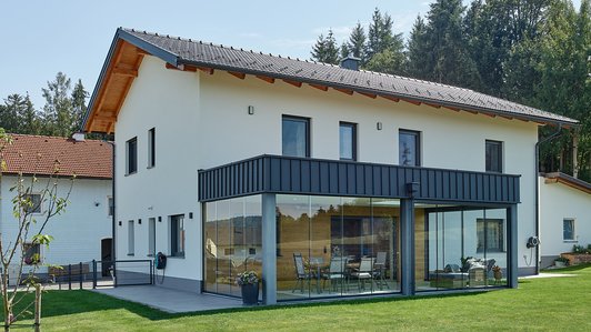 Massivhaus aus Ziegel und Holz mit Wintergarten - Außenansicht mit Wintergarten und Garten