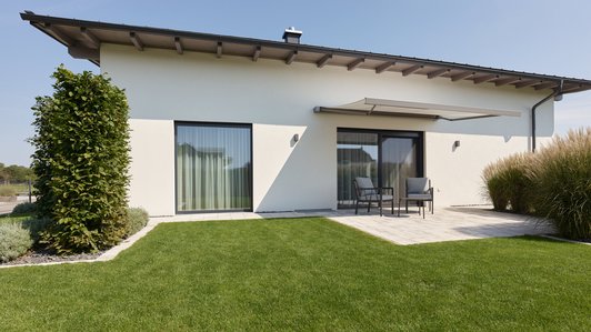 Gartenansicht des Flachdach-Bungalows mit großzügiger Rasenfläche