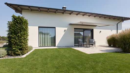 Gartenansicht des Flachdach-Bungalows mit großzügiger Rasenfläche