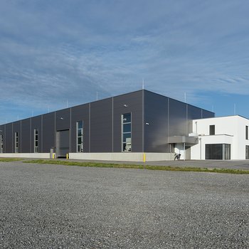Moderne Lagerhalle mit grauer Fassade und Nebengebäude, weitläufiges Areal mit leicht bewölktem Himmel