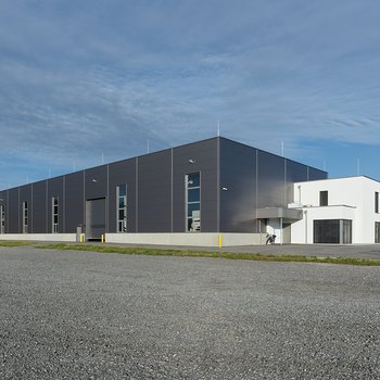 Moderne Lagerhalle mit grauer Fassade und Nebengebäude, weitläufiges Areal mit leicht bewölktem Himmel