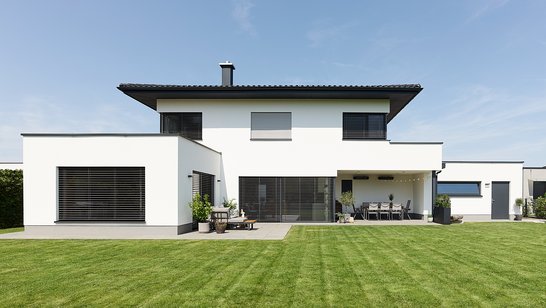 Rückansicht eines modernen weißen Hauses mit großen Fensterfronten und gepflegtem Rasen