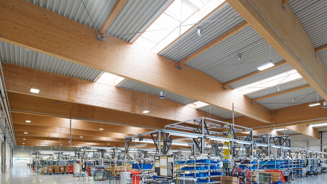 Innenansicht der Produktionshalle mit modernen Holzträgern an der Decke und einer Fertigungsstraße für Fahrerkabinen