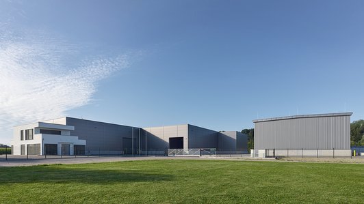 Blick auf zwei Lagerhallen mit Zufahrt und weitem Gelände, bei strahlend blauem Himmel